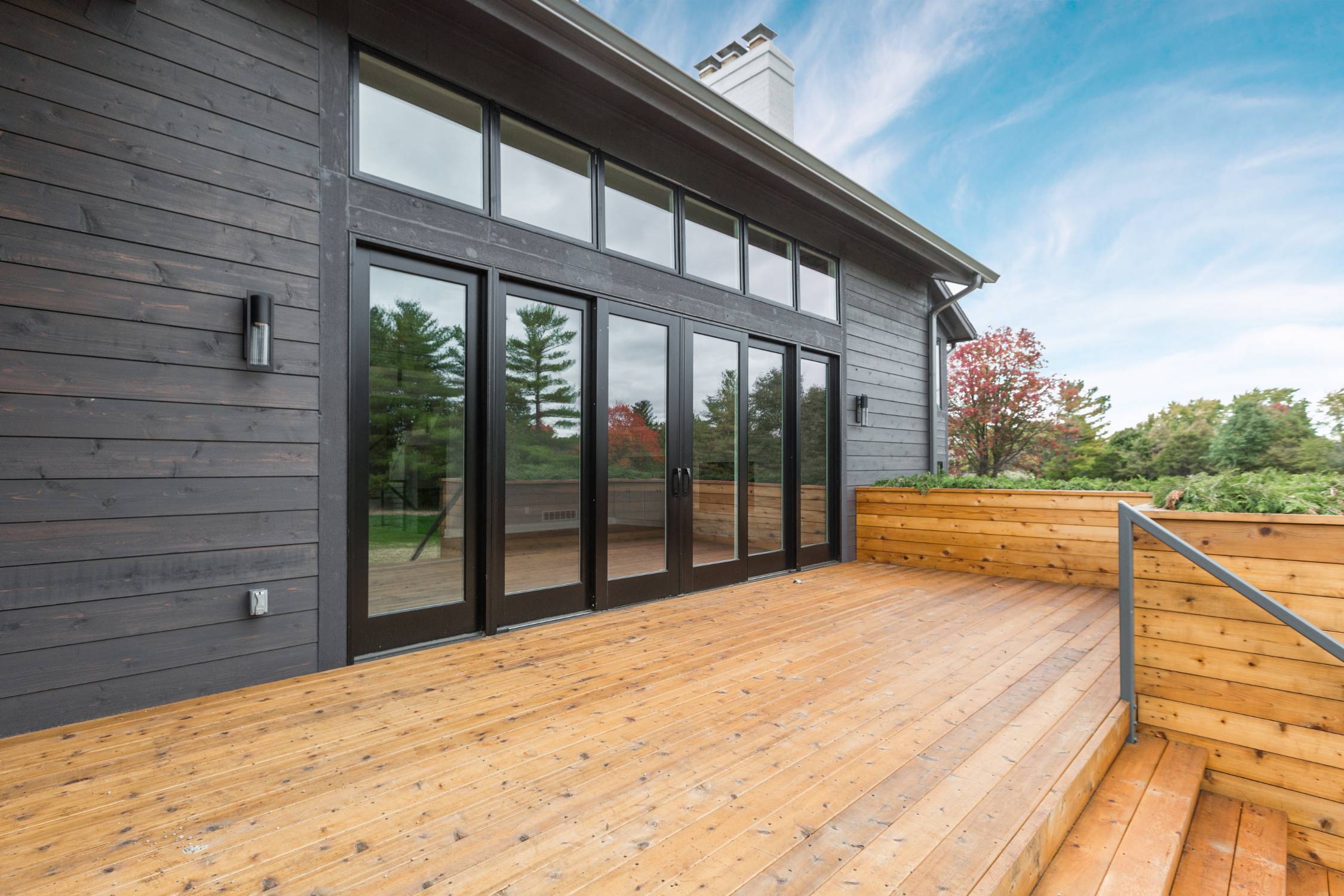 Modern custom home exterior with cedar deck, black-framed glass doors, and dark siding built by Eaton Custom Homes in Westfield